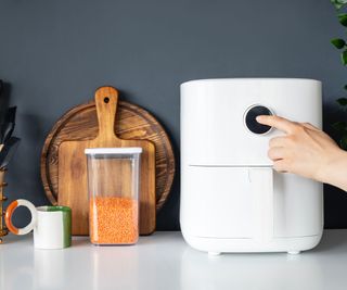 A white air fryer on a white countertop with wooden chopping boards and red lentils beside it