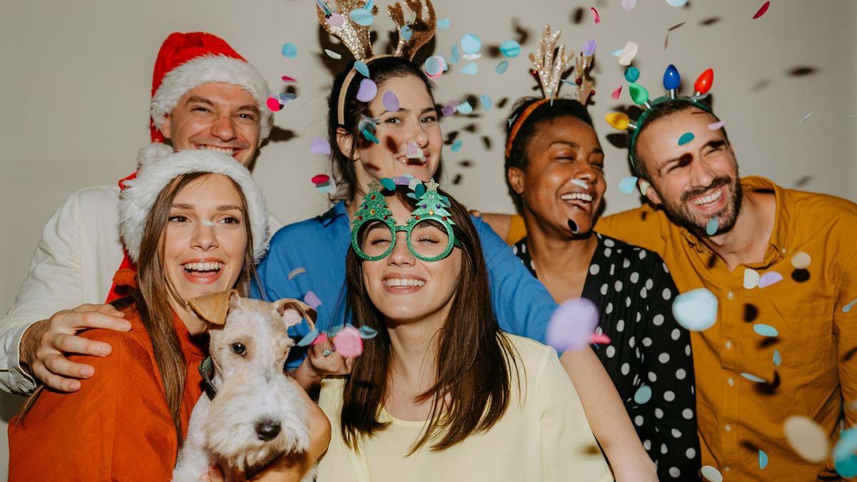 Six people and a dog celebrating New Year with confetti and wearing festive hats