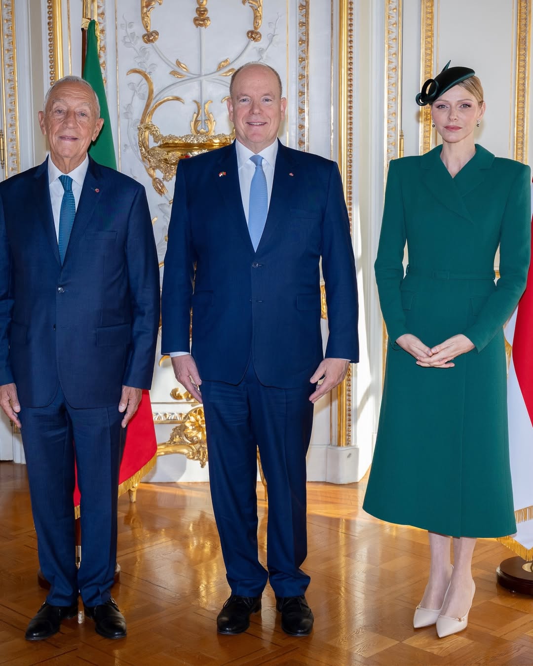 Princess Charlene in a green coat dress and Prince Albert wearing a blue suit, posing with the president of Portugal