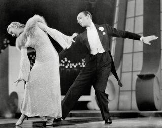 a woman in a long furlined dress and a man in a tux dance together in the movie Top hat