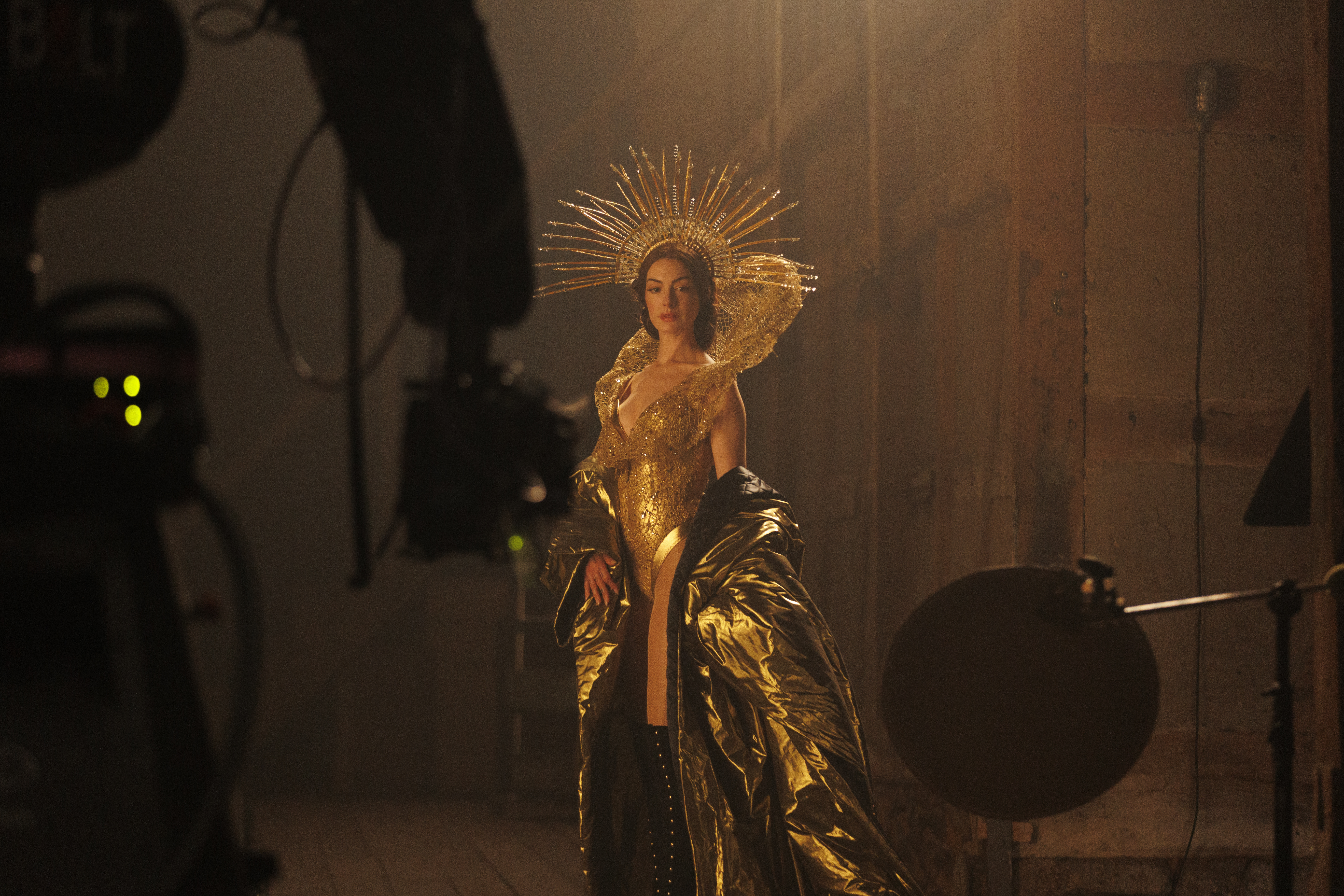 anne hathaway as a pop diva in a gold ensemble including a crown posing for cameras on a set in a still from the movie mother mary