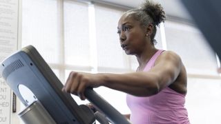 A woman with grey curly hair uses an elliptical trainer to work out her upper body and legs