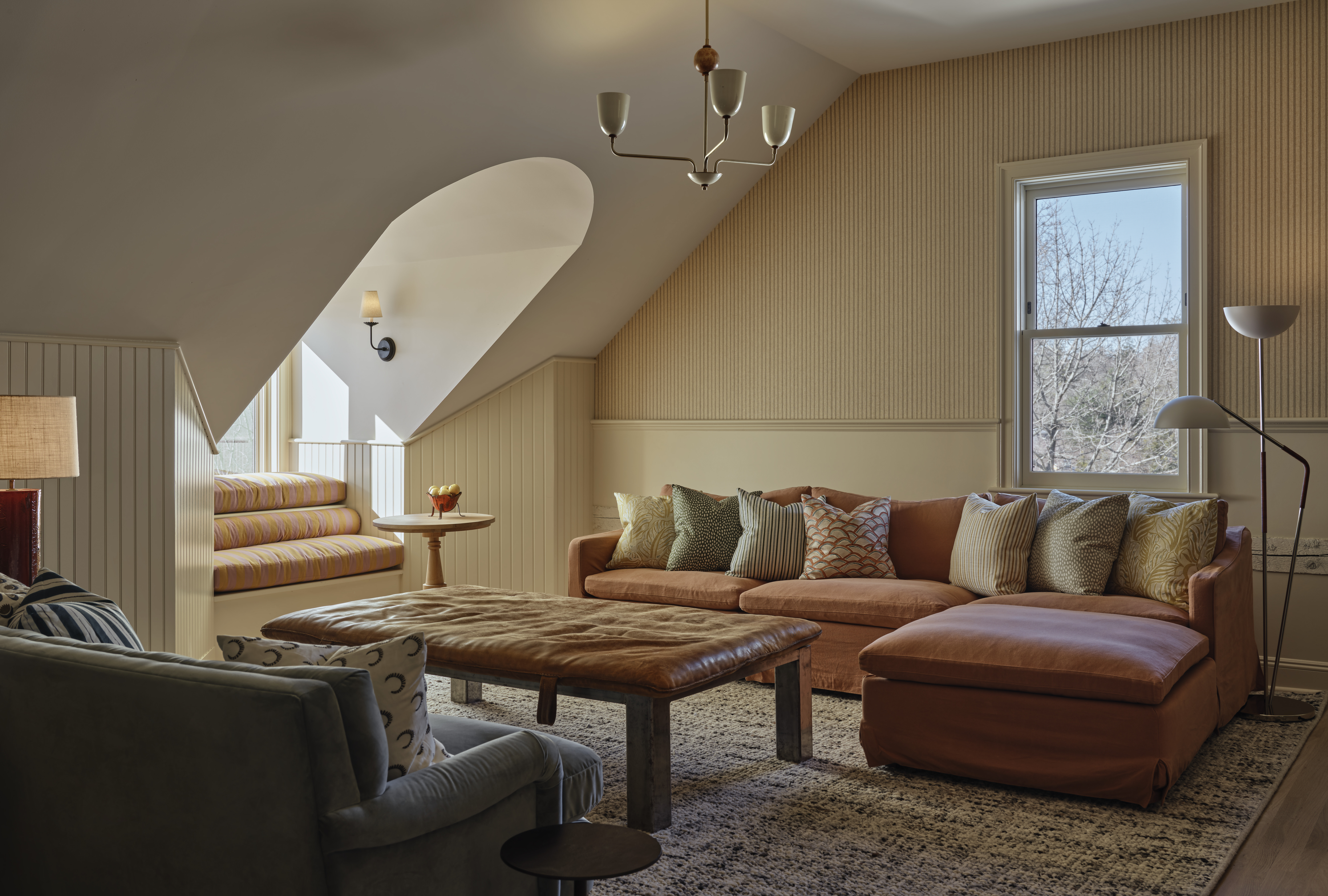 A cocooning, contemporary hotel features 1970s-inspired, plush, and puffy furniture, including upholstered modular sofas, shearling-topped chairs, and leathery chaise longue, sculptural lighting, and wooden tones mixed with vibrant greens.