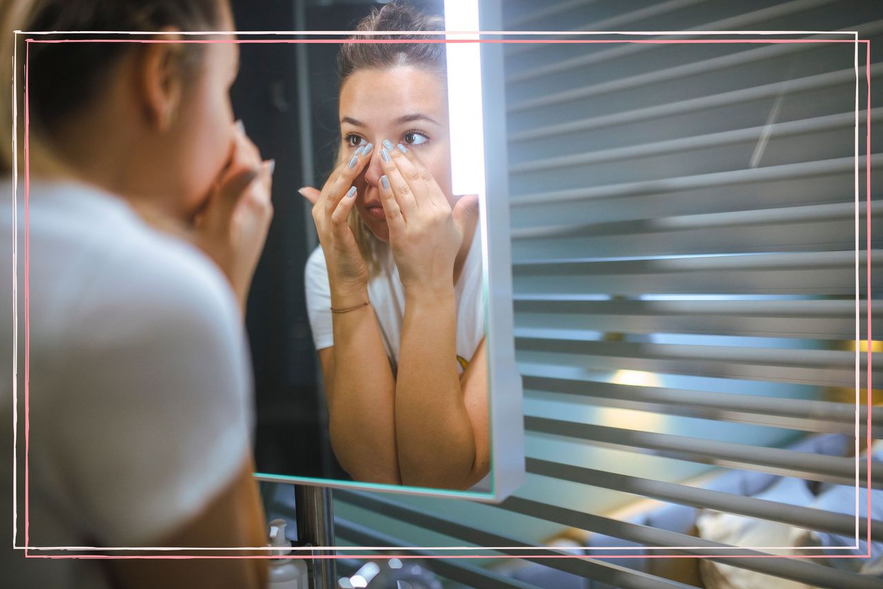 A woman looking in a mirror and touching under her eyes