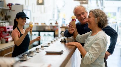 An older couple smile at each other while getting ice cream in an ice cream shop.