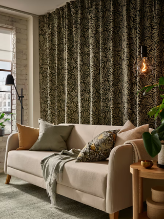 A living room with a sofa with patterned cushions and floral printed curtains in the background