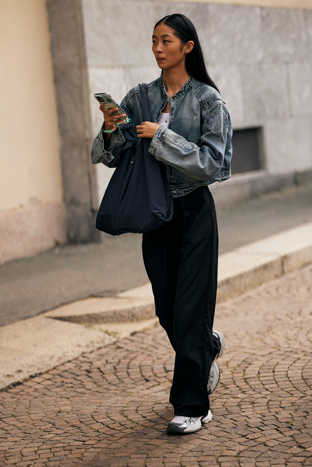 Fashion week attendee wearing tote bag, denim jacket, black pants, and sneakers