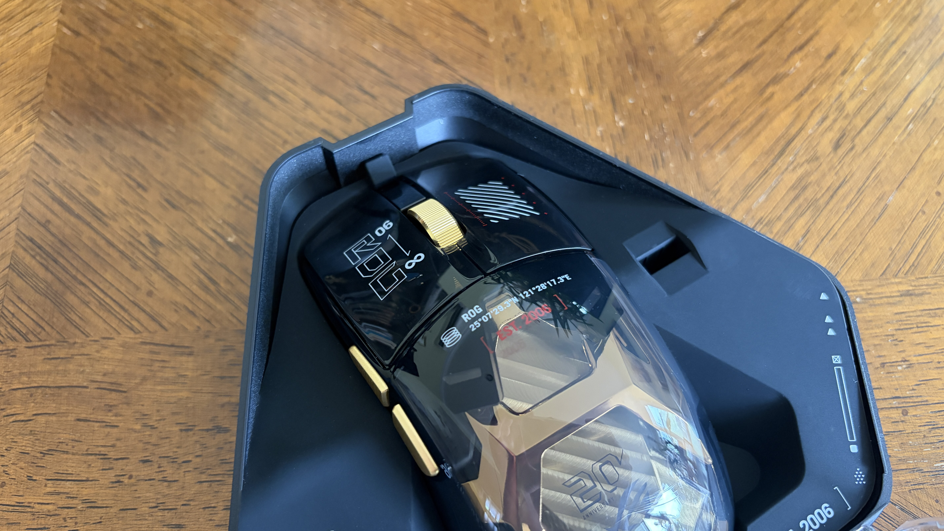 A glossy black ASUS ROG gaming mouse with gold accents partially in its packaging on a wooden surface.