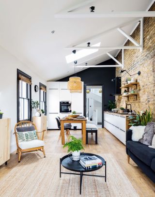 An open-plan living room with high ceilings, dining room table with chairs and bench and exposed brick wall