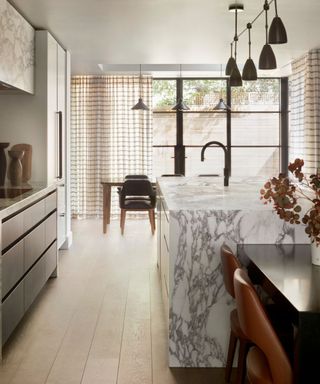 A kitchen with a marble island, floor-to-ceiling windows and a small dining area