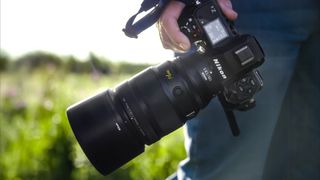 Nikon Z 135mm f/1.8 S Plena lens held in a hand in a field