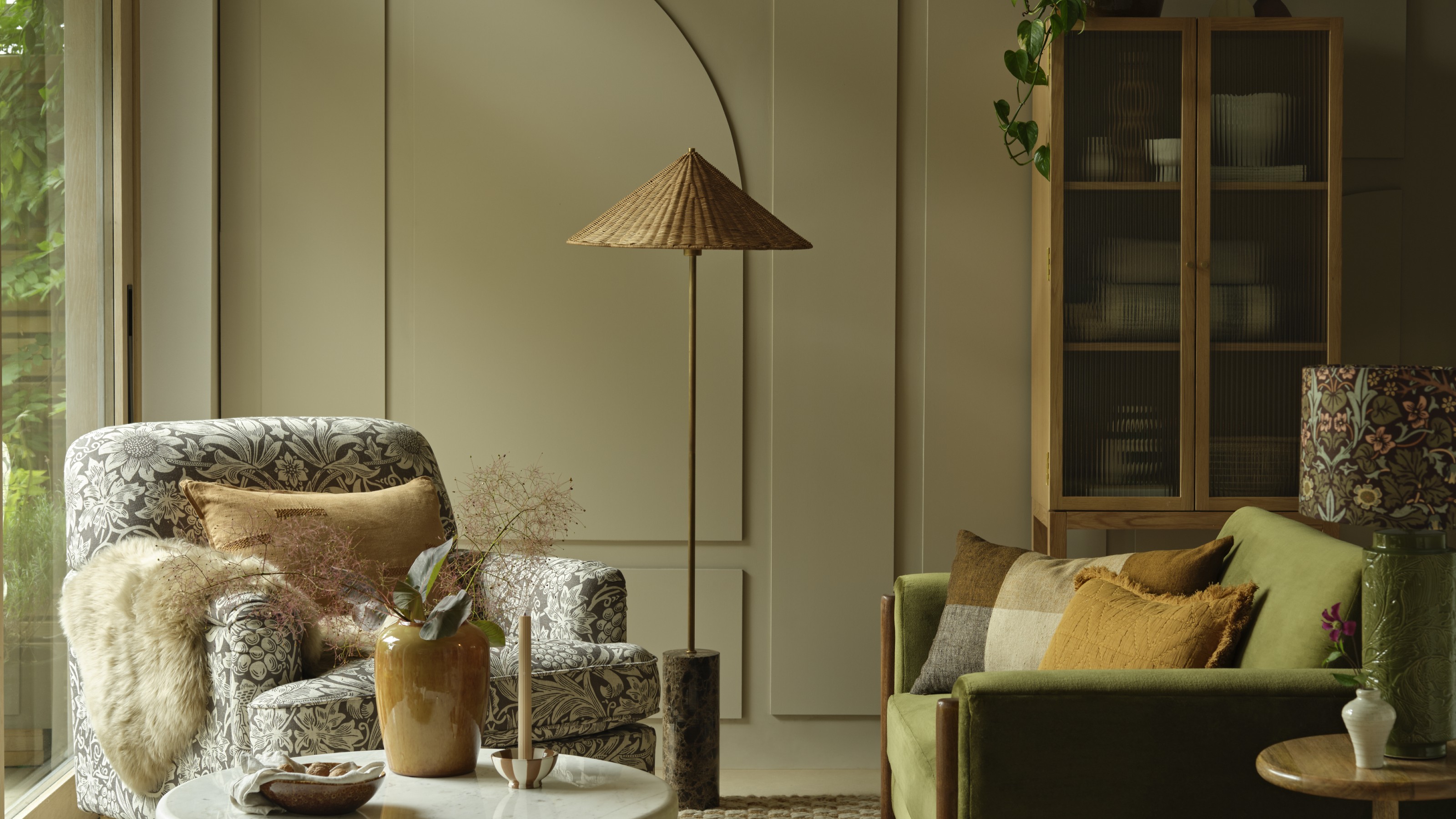 A living room with a panelled beige-painted wall, a Morris &amp; Co.-print armchair and a green velvet sofa
