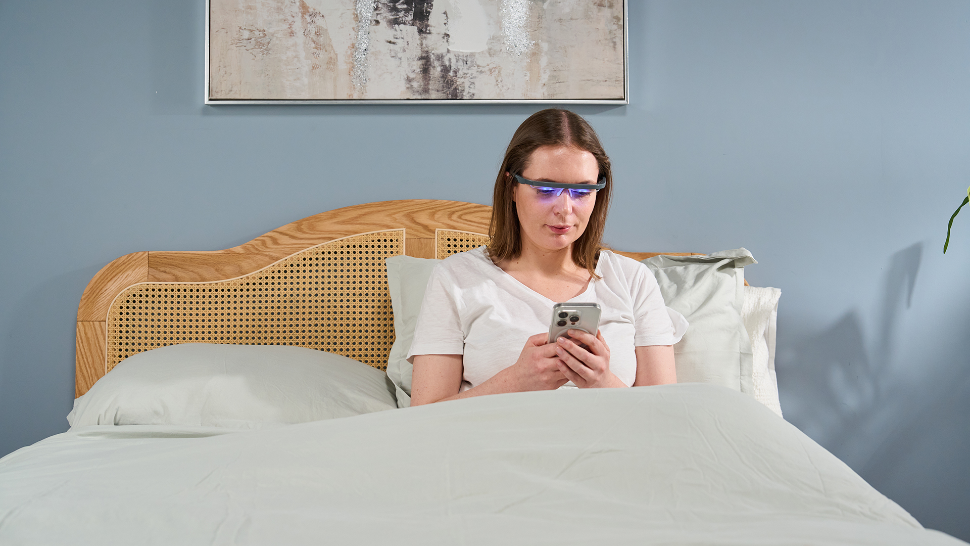 A Tom's Guid sleep tech tester sits up in bed while wearing the AYO+ Blu Light Therapy Glasses