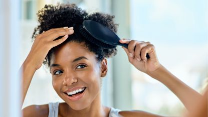 best hair brush - woman smiling in the mirror brushing her hair - gettyimages 1149196482