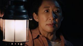 Sandra Oh stands with a lantern near her face in Umma