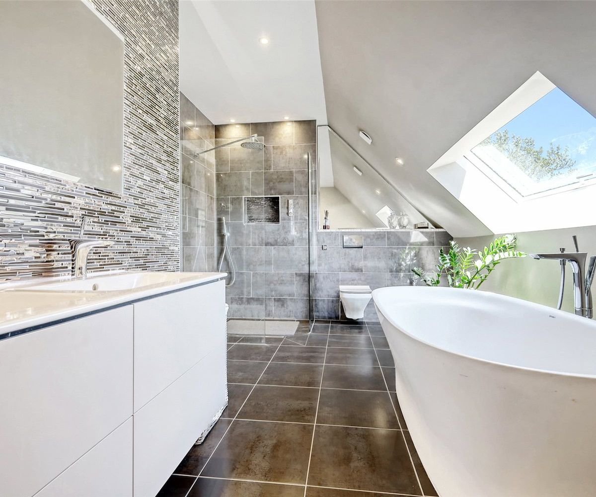 A bathroom with a slanted ceiling and black ceramic floor tiles and a rooflight
