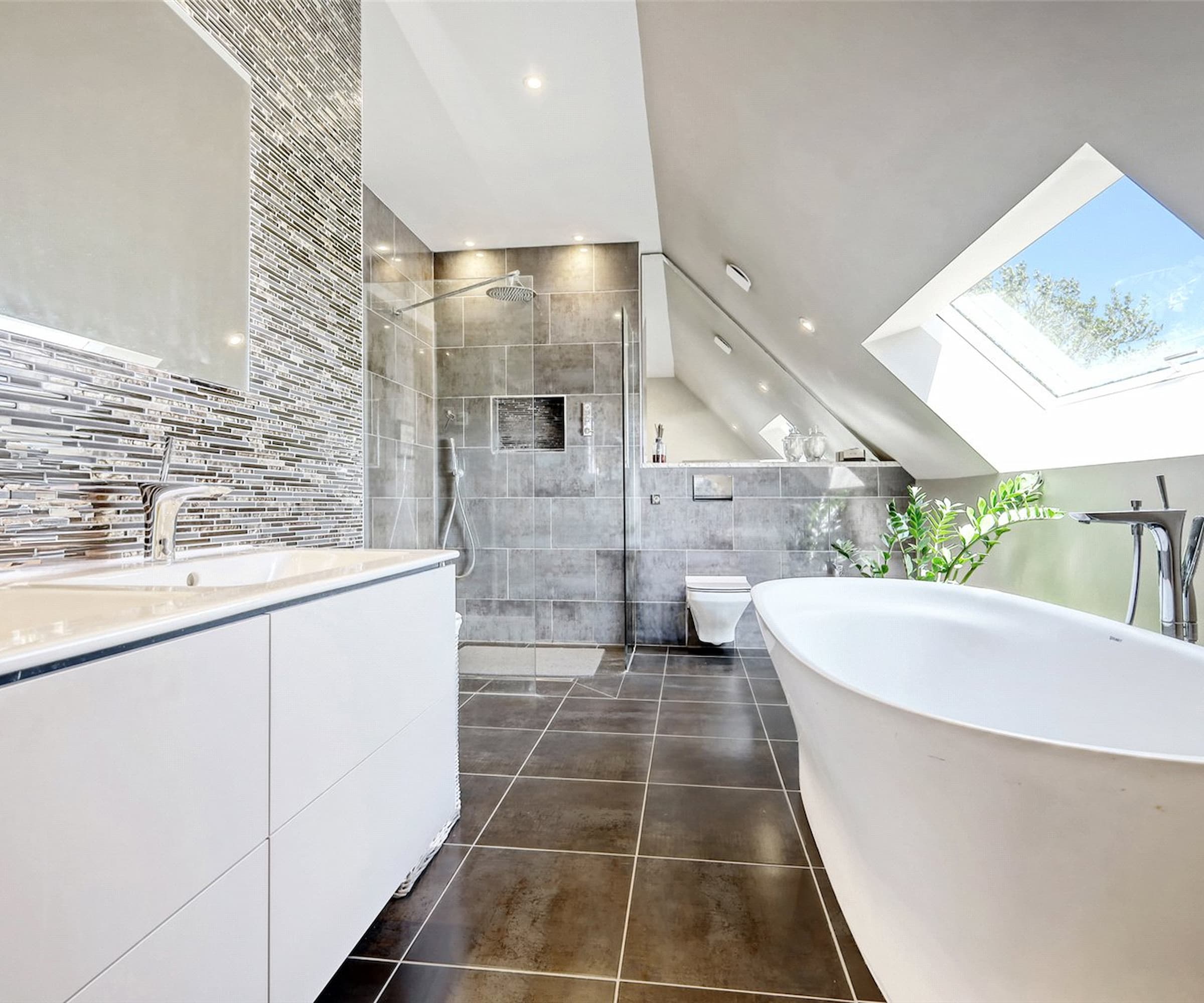 A bathroom with a slanted ceiling and black ceramic floor tiles and a rooflight