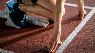 The legs and arms of a male athlete are shown as he is crouched down at the start line ready to begin a race.