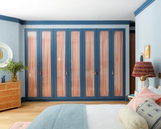 colorful bedroom with red fabric backed glass paneled built in wardrobe, blue walls, blue throw, wooden floor and patterned cushions