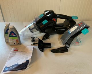 Pre-assembly image of the Bissell Pet Stain Eraser Duo portable carpet cleaner with bottles of cleaning solution and instruction manual
