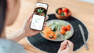 Woman's hands holding calorie counting app on phone with bowl of salad sitting on table