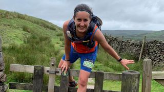 A woman in trail running gear climbs over a stile mid-race.