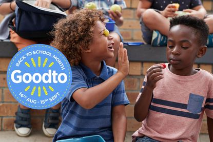 Two boys laugh while eating and playing with fruit from a lunch box