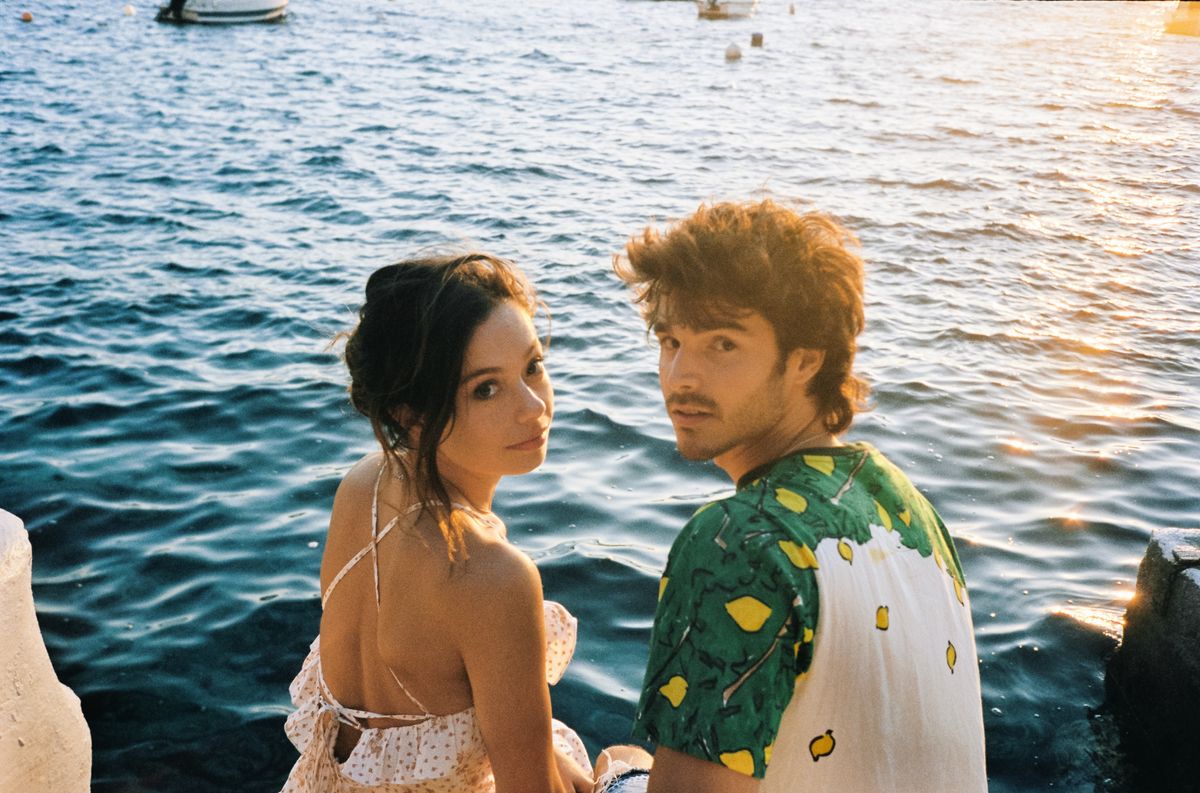 Margot and David look up at the camera with the sea behind them.