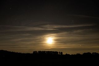 The moon lighting up cirrus clouds above a silhouetted landscape