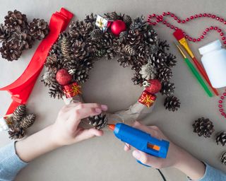 top view of florist's hands, Christmas wreath of fir cones, decorative toys and ribbon