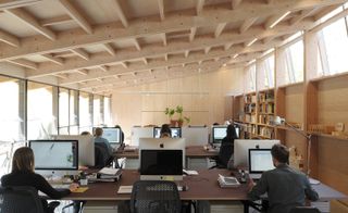 A photo of a library room with twelve iMac computers and students using them. The room has a slanting wood roof and window providing light from either side of the room.