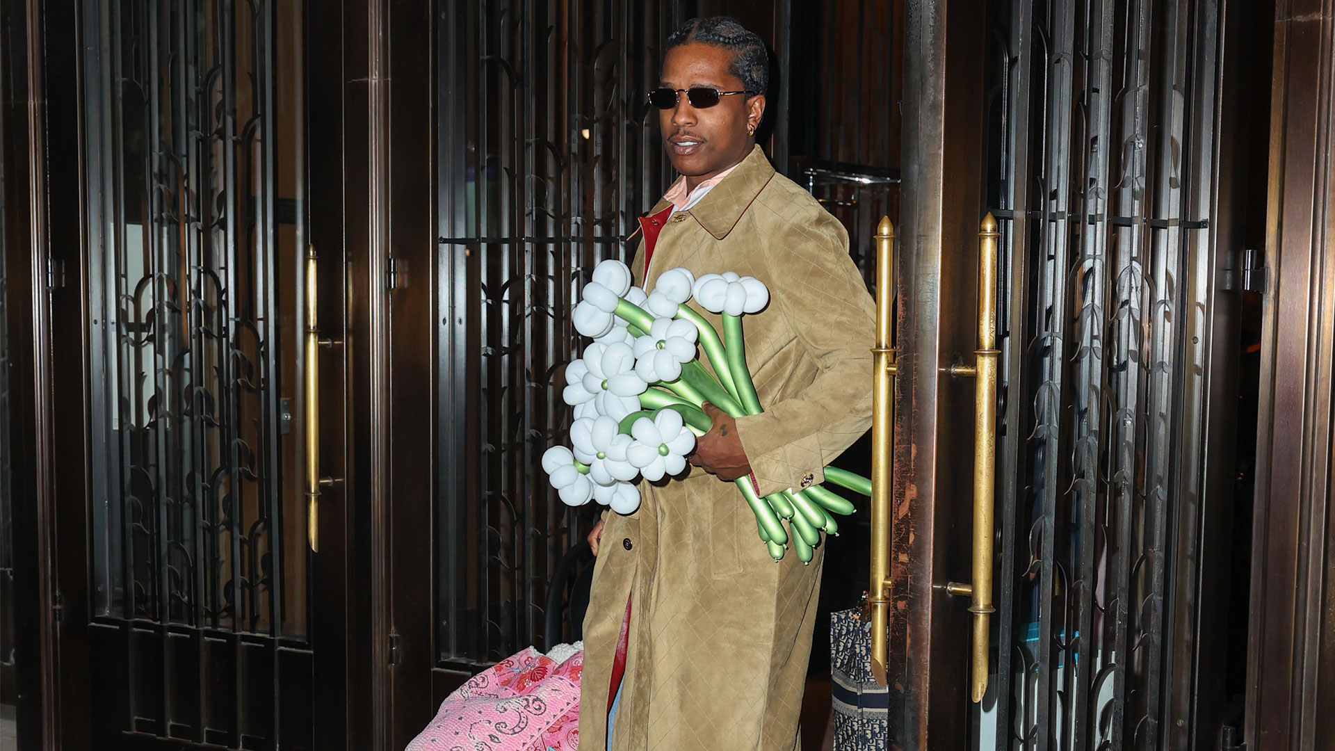 ASAP Rocky seen holding a car seat with pink blanket over it and bouquet of flowers.