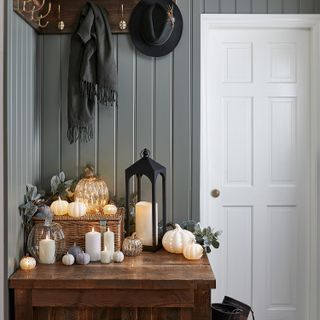 grey hallway with table full of pumpkins, candles, lantern, basket with lit pumpkin on top, peg rail with scarf and hat