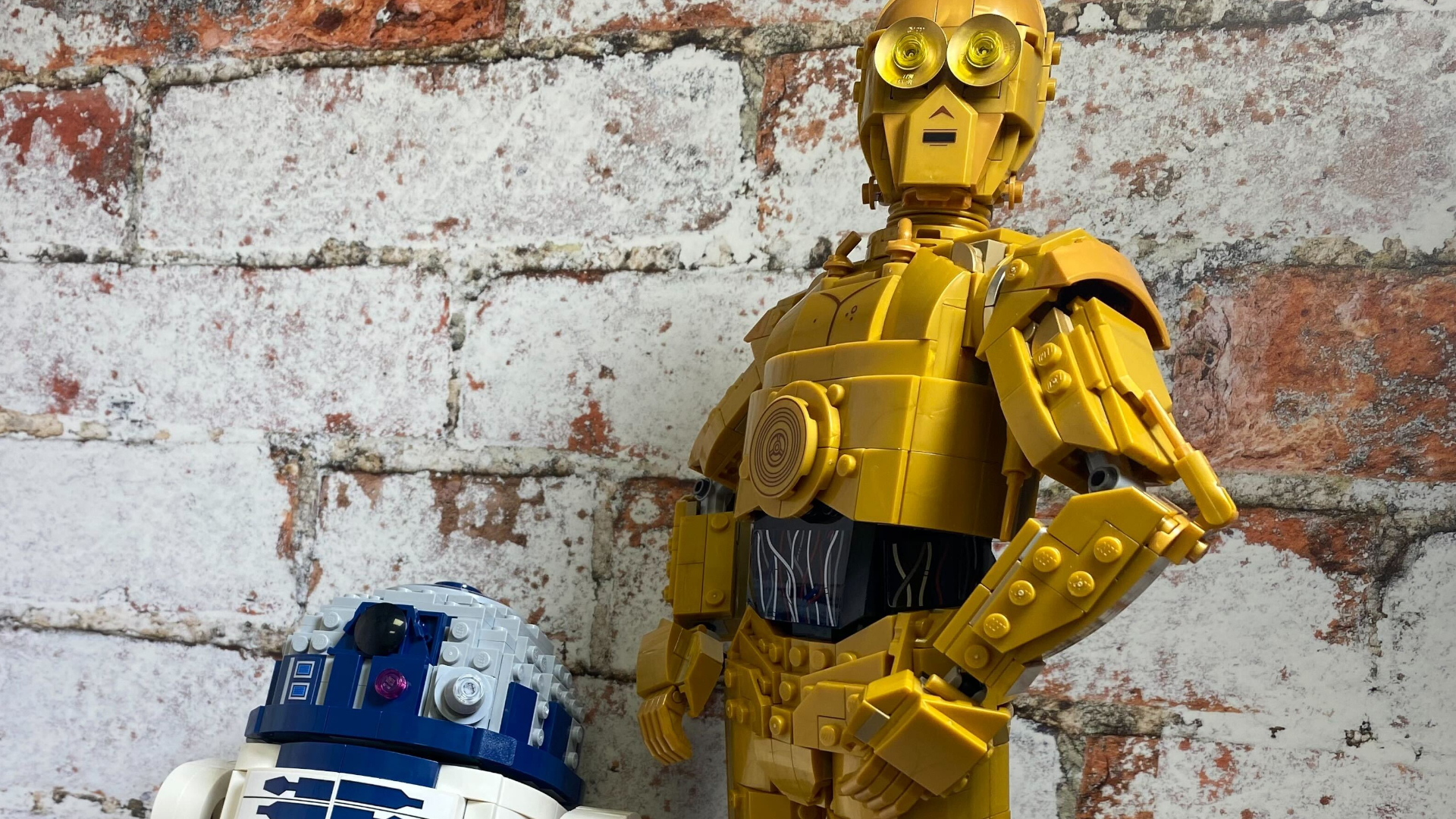 Lego C-3PO y Lego R2-D2 uno al lado del otro en una pared de ladrillos