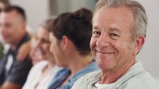 An older man sits in a group staring out at the camera.
