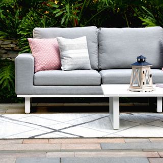 Soft grey sofa outside with cushions and rug on floor