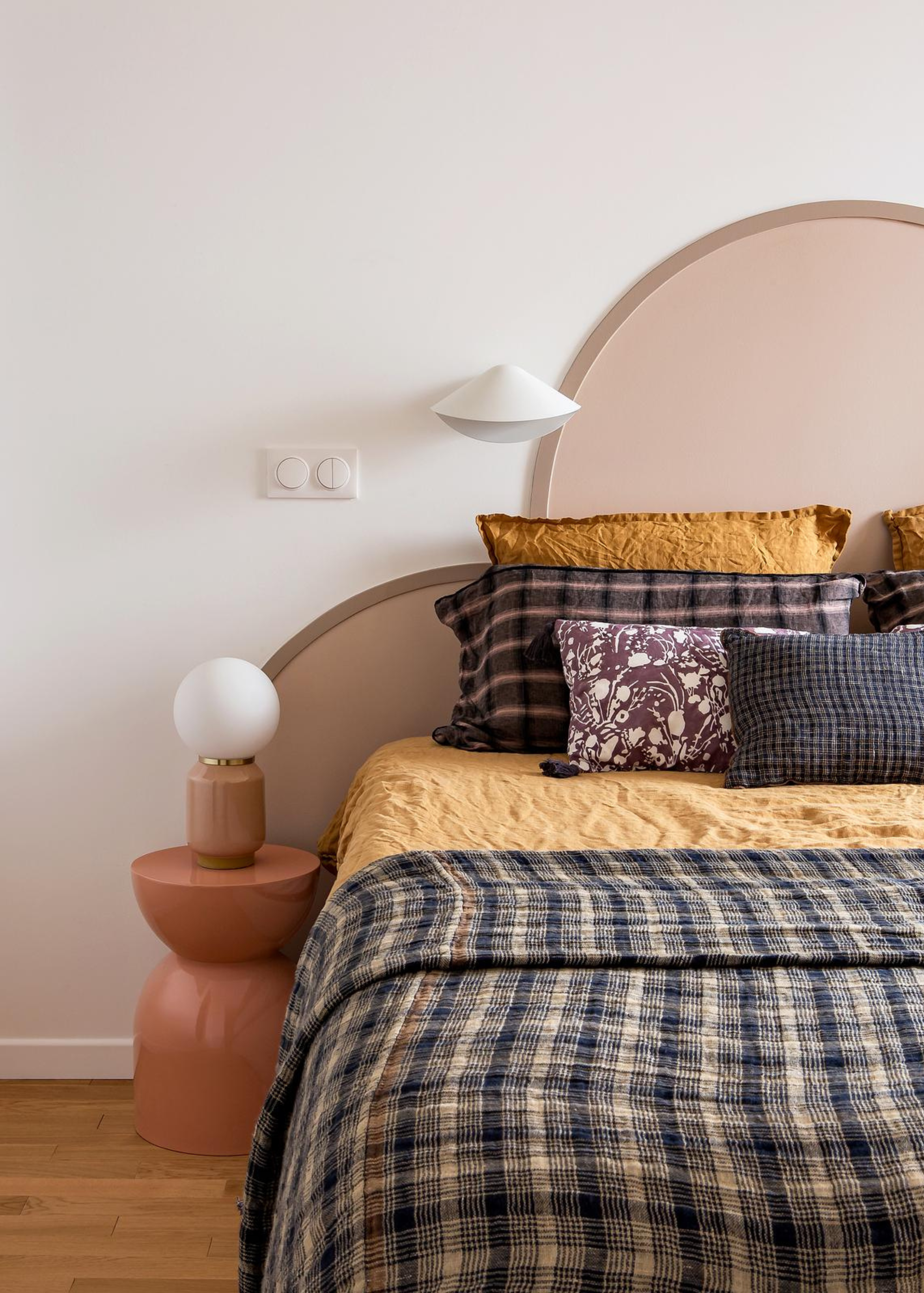 A bedroom with a curvy headboard and layered patterned pillows