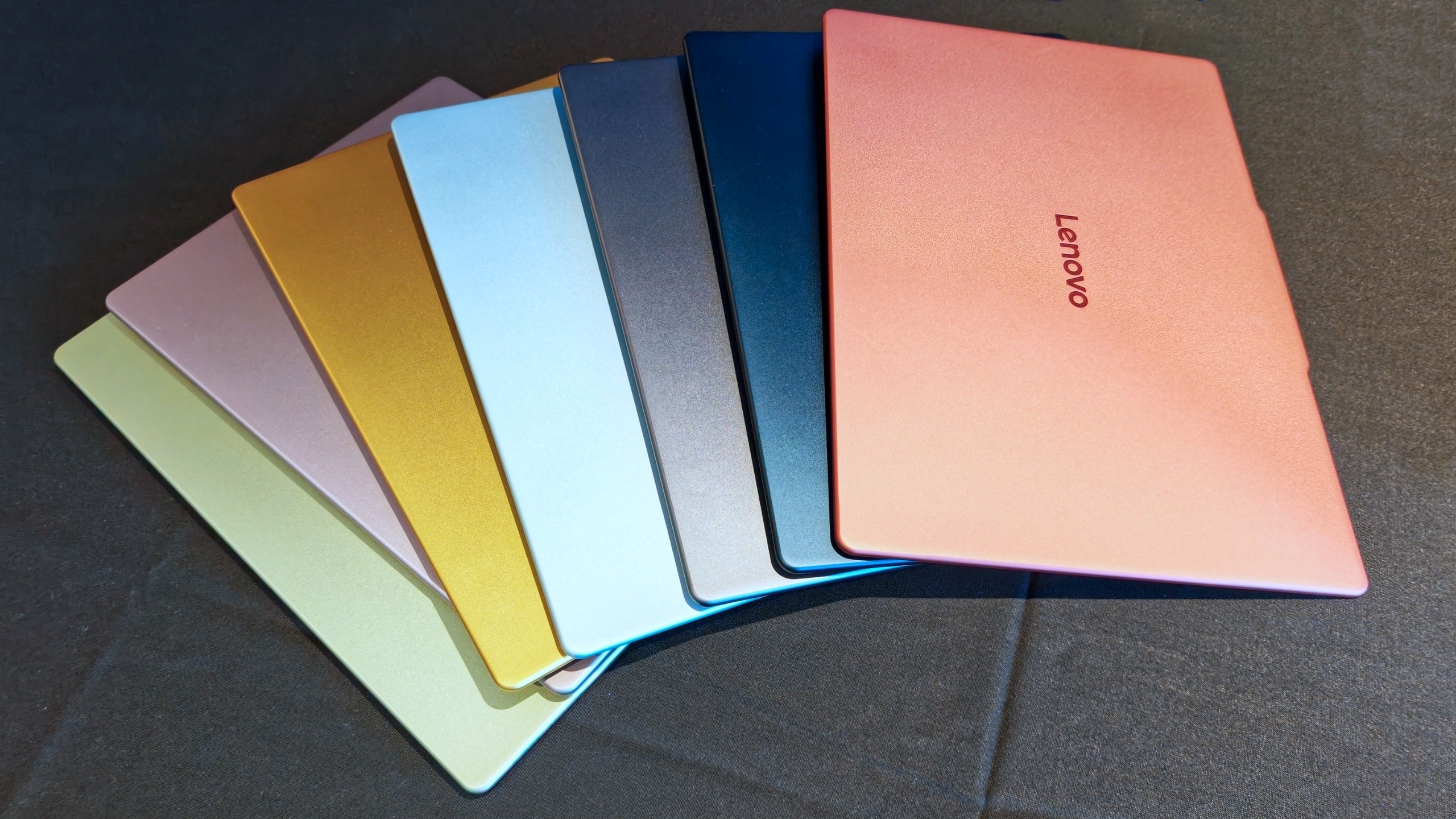 Fan-like arrangement of seven Lenovo IdeaPad Vibe laptop top lids displaying a full spectrum of color options.