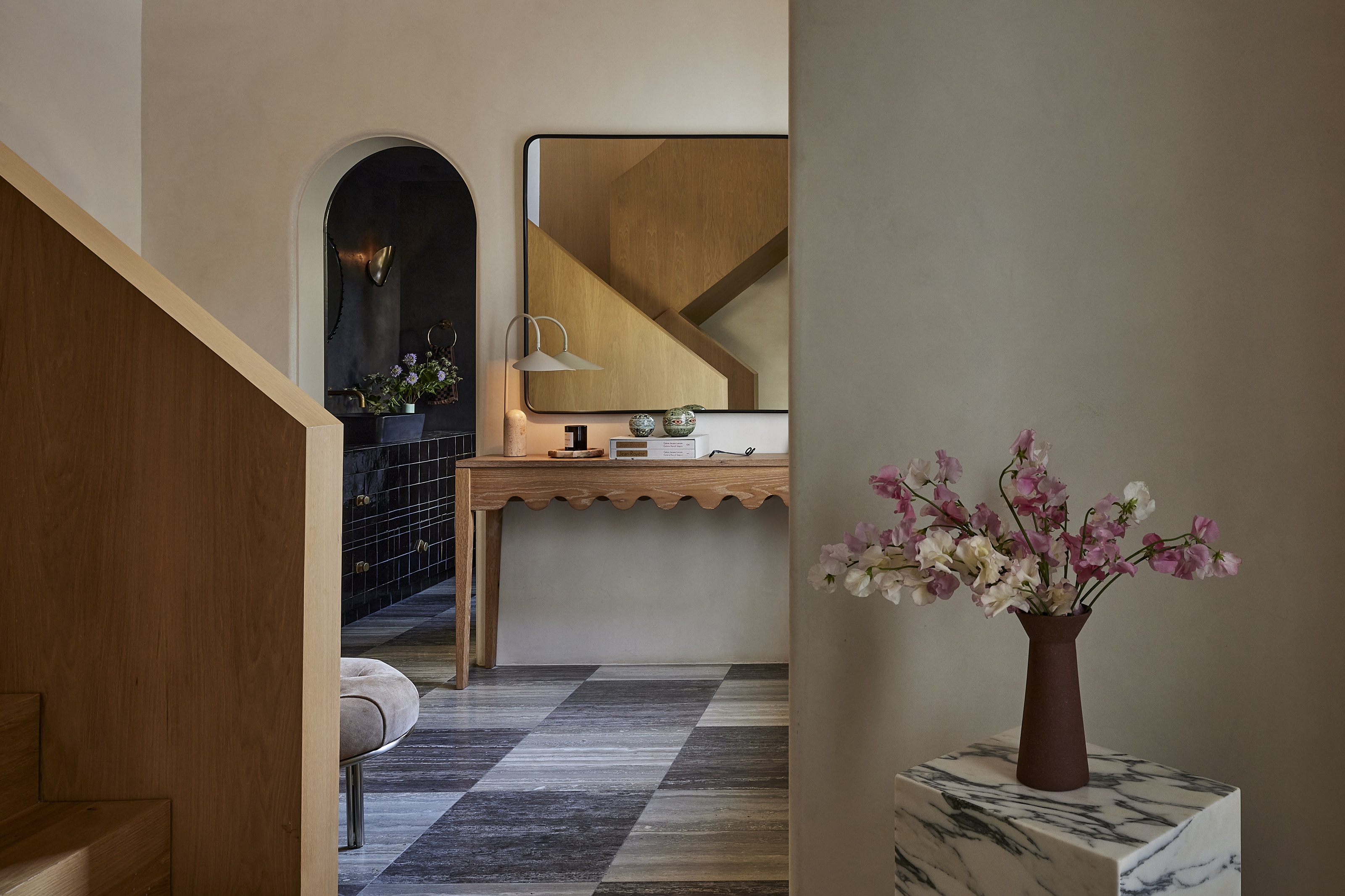 an entryway with a checkerboard floor, wavy console unit, and marble plinth