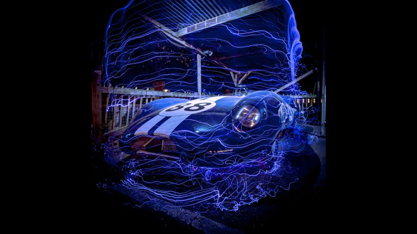 A sleek blue race car with the number 38, surrounded by swirling blue light streaks, in an illuminated nighttime setting.