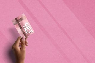 A person holding a pink gift card in front of a pink background.