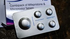 Close-up image of a silver packet of mifepristone and misoprostol pills with the white box behind it