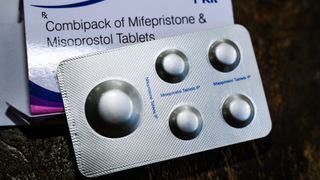 Close-up image of a silver packet of mifepristone and misoprostol pills with the white box behind it