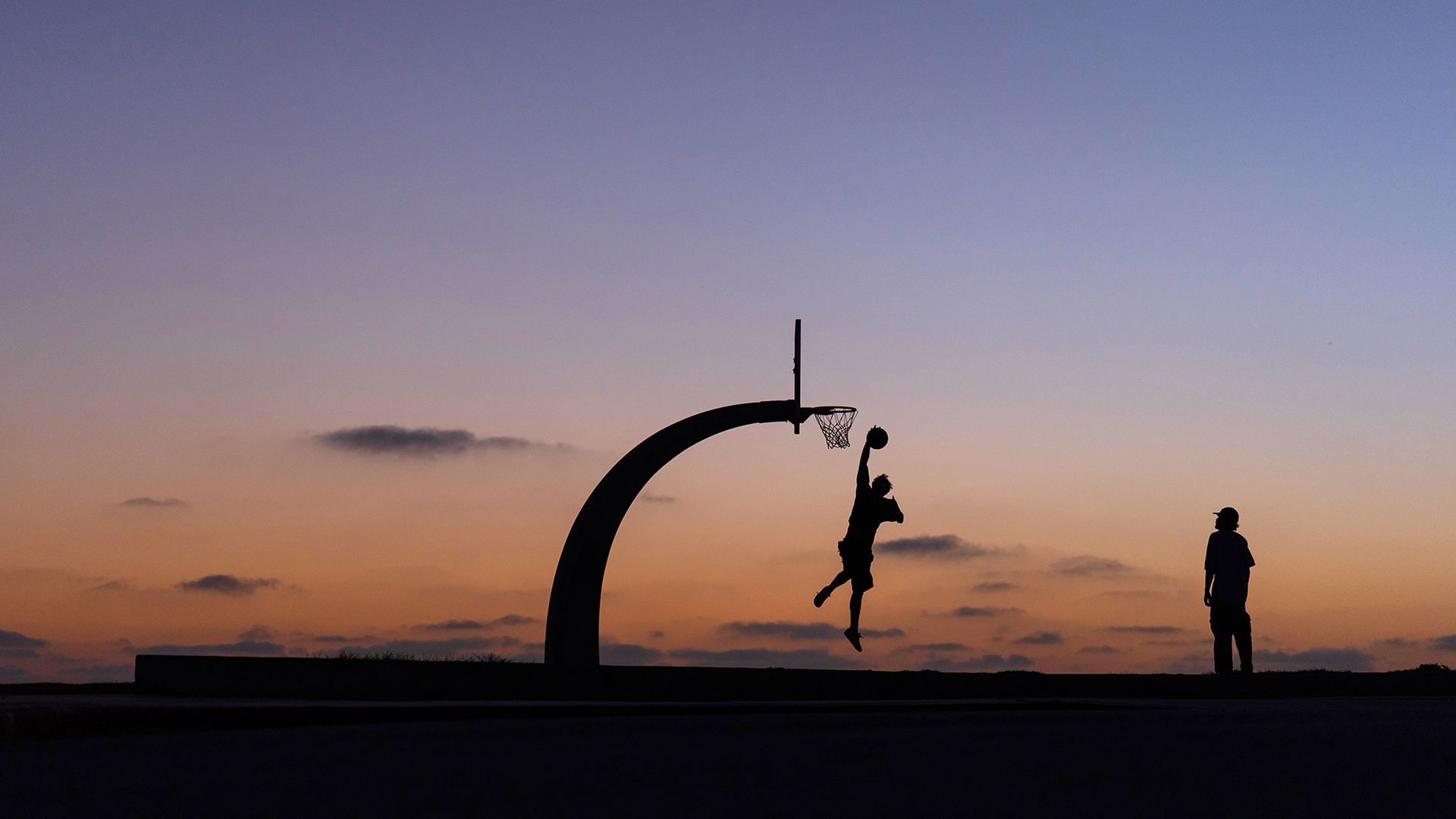 
                                Two people are silhouetted playing basketball at dusk in the San Pedro neighborhood of Los Angeles
                            