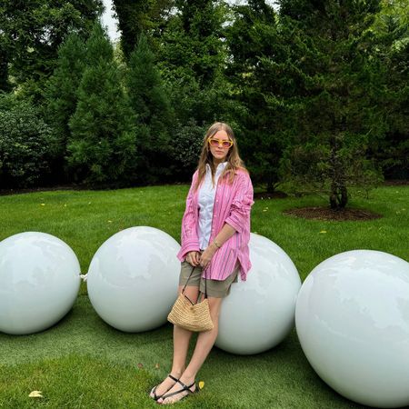 Nikki Chwatt wears green bermuda shorts from Zara, a pink striped button-down, white button-down, yellow sunglasses and a straw shoulder bag.