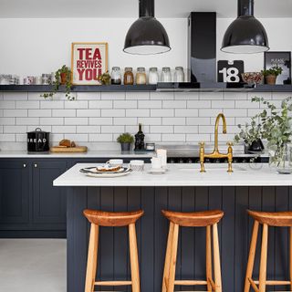 Kitchen with black panelled island, white metro tiles, wooden bar stools and metal pendant lighting