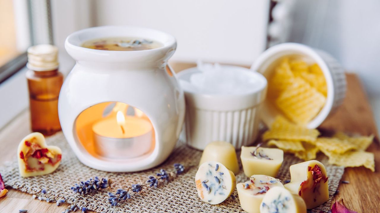 A white wax warmer with a lit candle beneath, with other solid wax blocks beside it. 