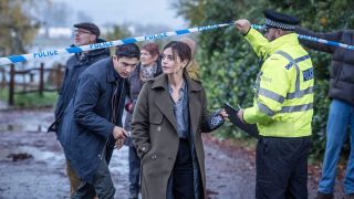 Detectives Hitch (Archie Renaux) and Ember (Jenna Coleman) duck under police tape at a crime scene in The Jetty