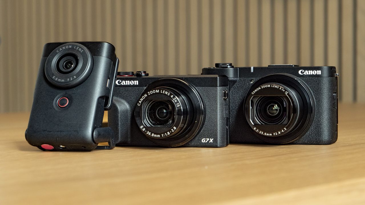 Canon PowerShot V1 compact vlogging camera on a wooden desk alongside the PowerShot G7X Mark III and PowerShot V10
