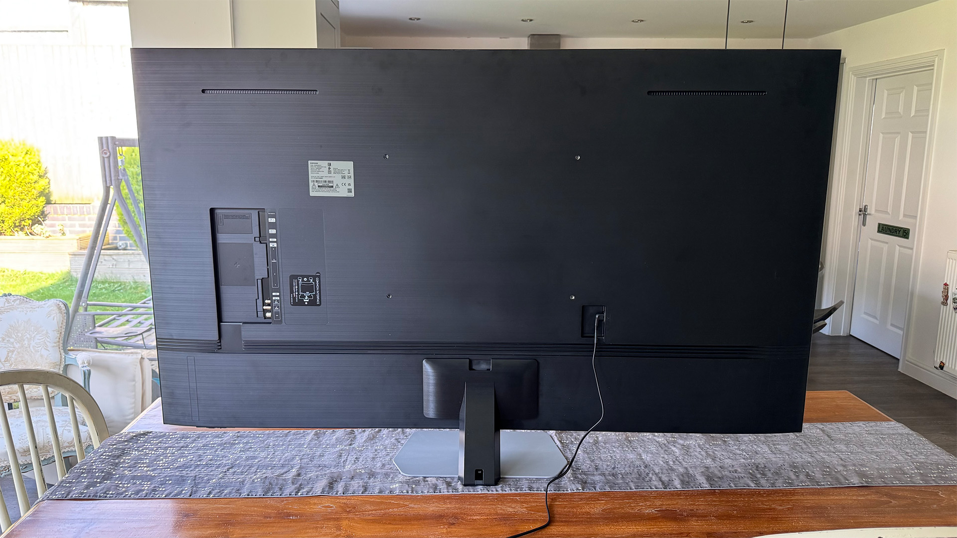 Samsung QN90F Mini LED TV on wooden dining table, rear of set
